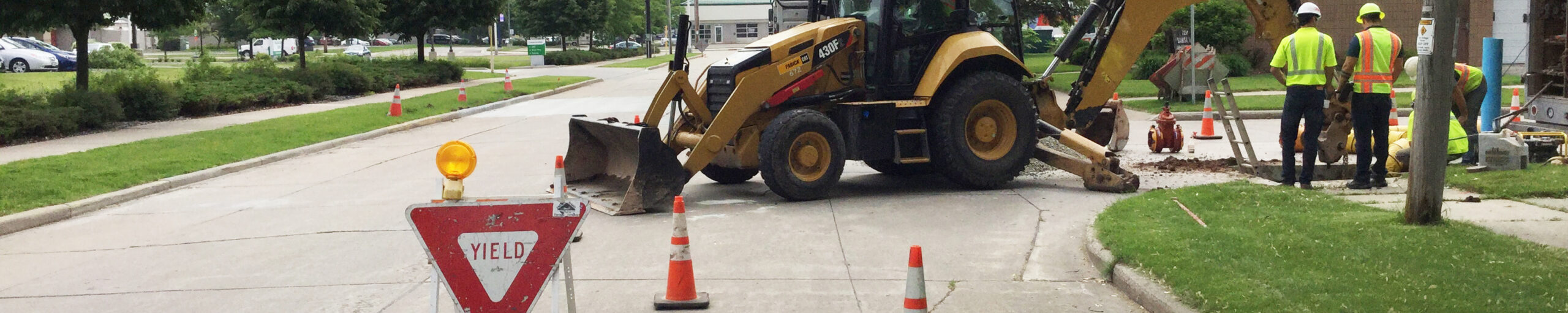 Road crew with a back hoe looking into a hole in the road